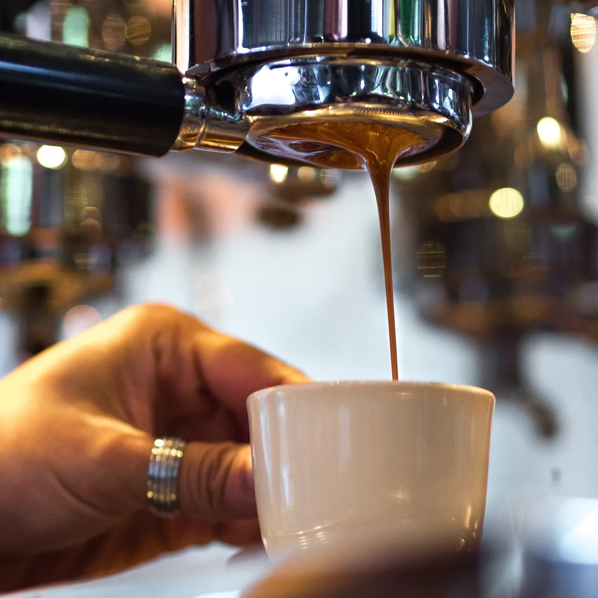 Espresso falling in a single stream from a bottomless portafilter into a small cup held underneath