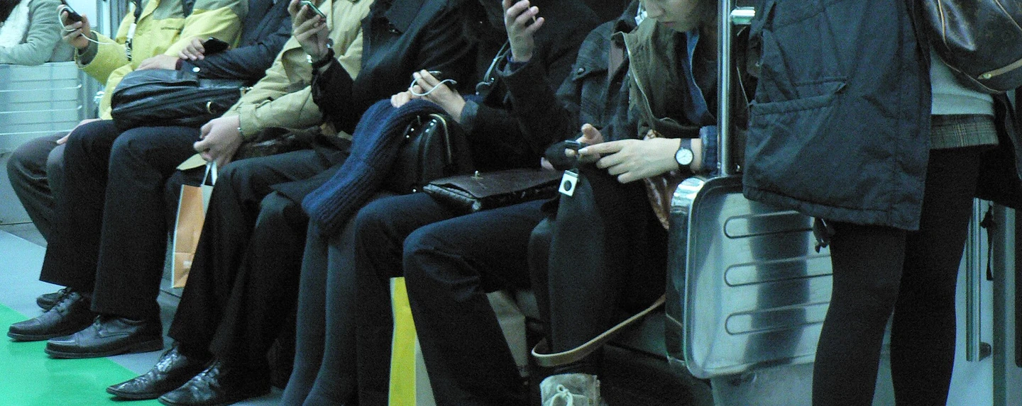 Hands and knees of passengers looking at their phones on the Seoul subway. The commute is when personalized briefings are consumed the most (2010, photo by Marc Smith, CC BY 2.0, via Wikimedia Commons; cropped to avoid showing faces)