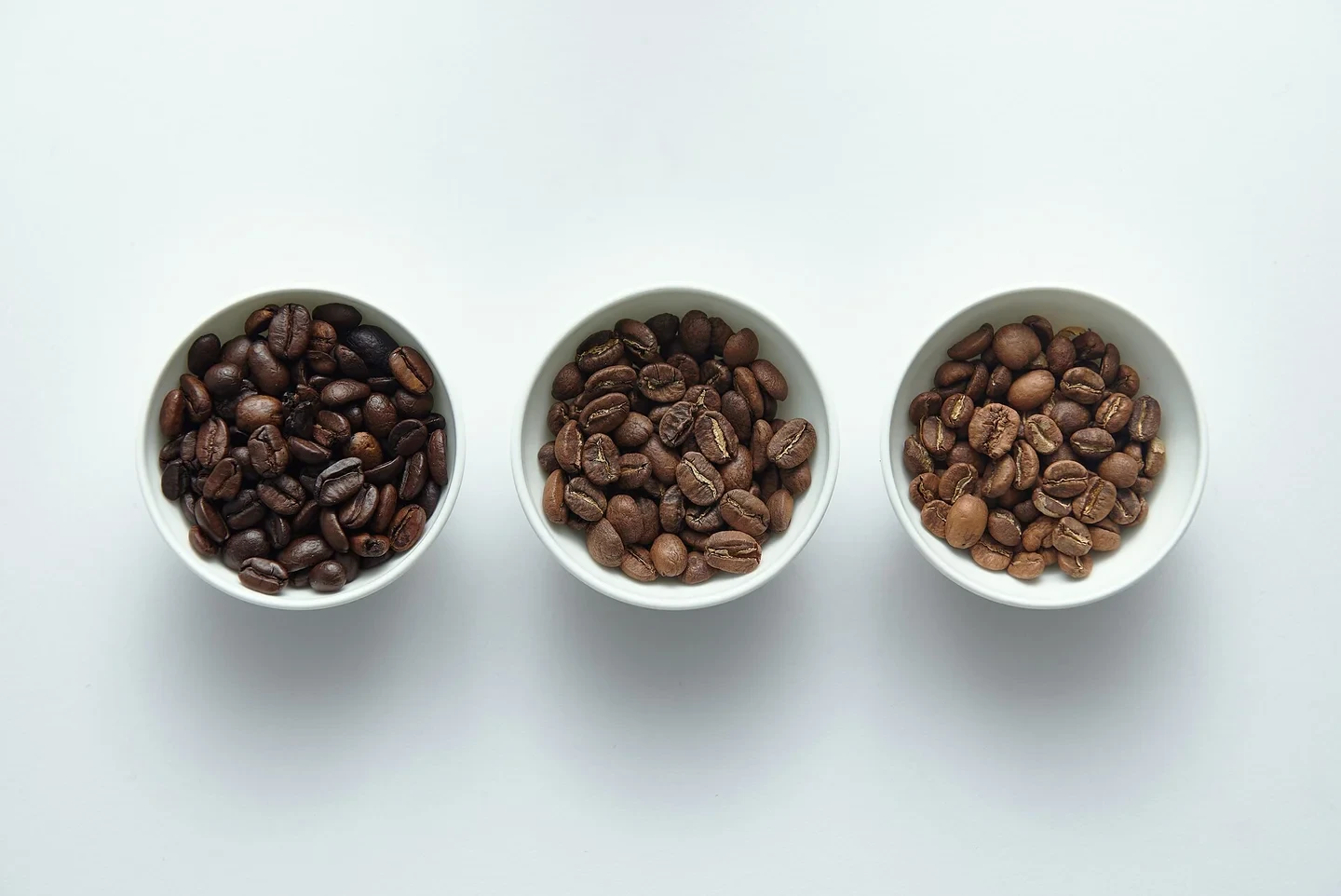 Three white bowls each holding 15 g of coffee beans. The one on the left is dark brown, roasted heavily, and the color lightens moving to the right