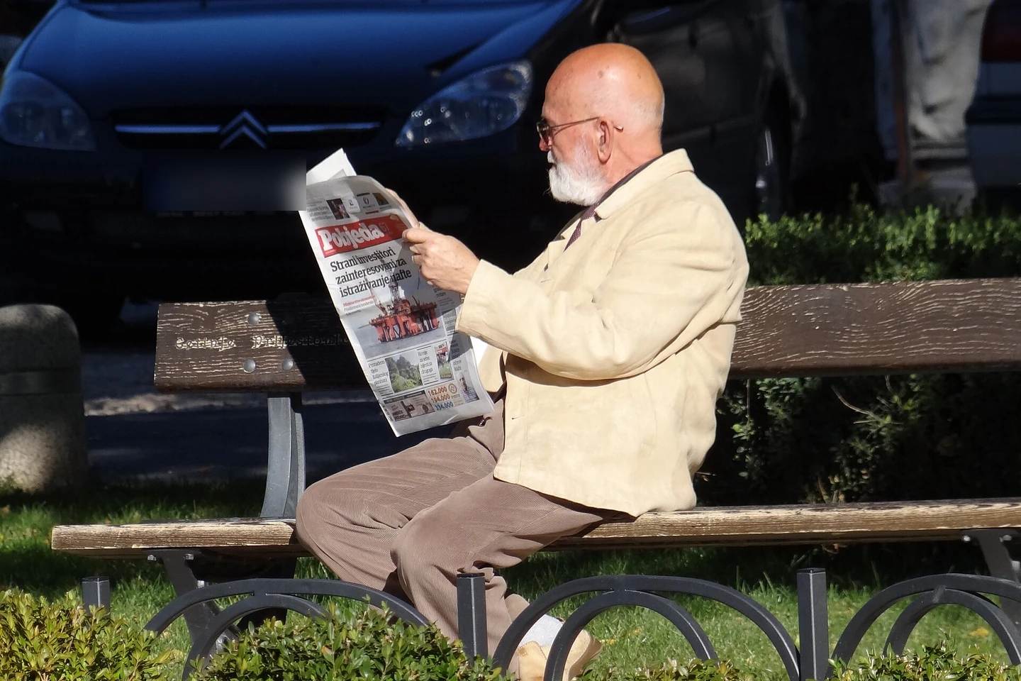 A man reading a newspaper on a park bench in the morning (Cetinje, Montenegro, 2012, photo by Adam Jones, CC BY-SA 3.0, via Wikimedia Commons)