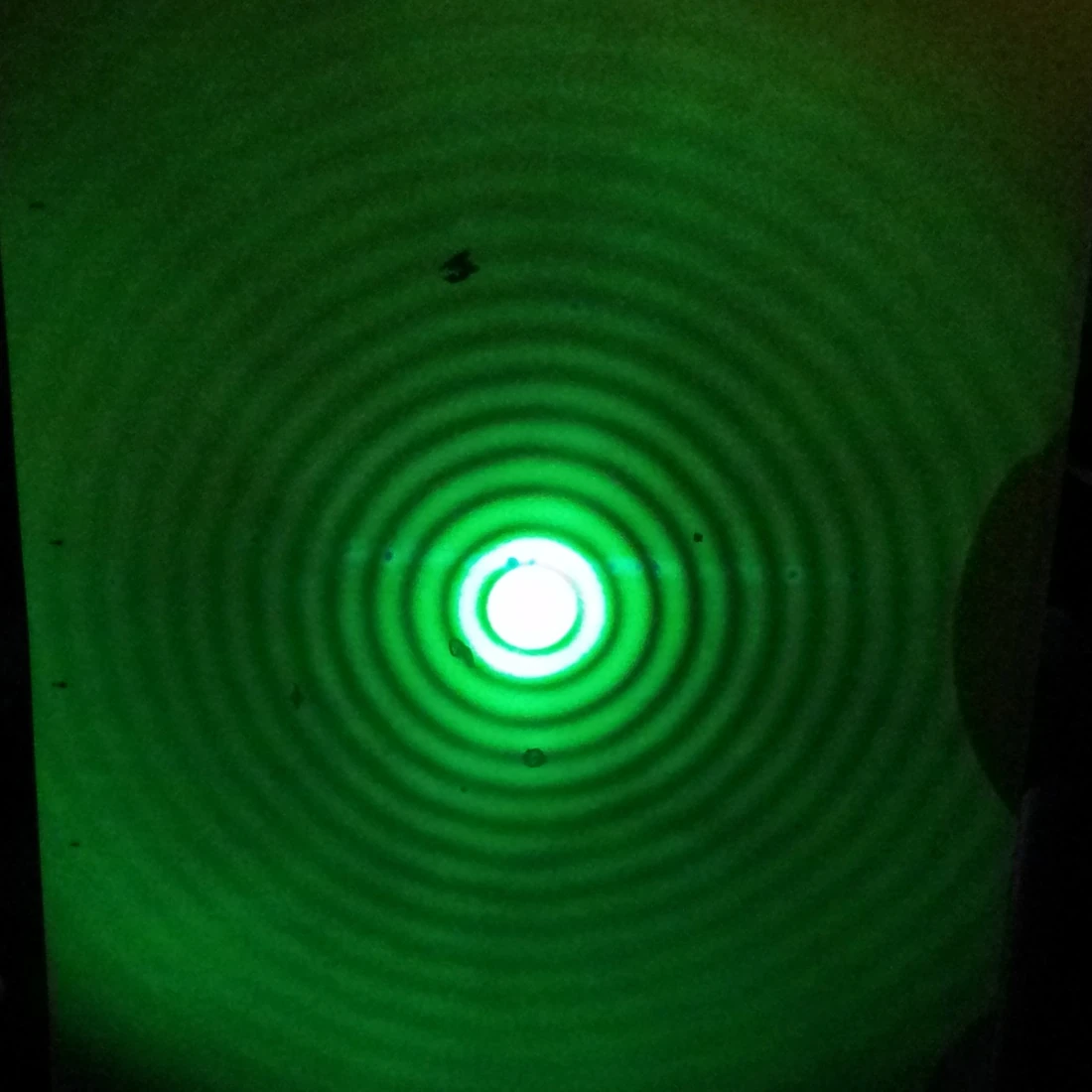A board lit by green light showing concentric rings on a dark background: a bright central disc surrounded by many alternating bright and dark rings