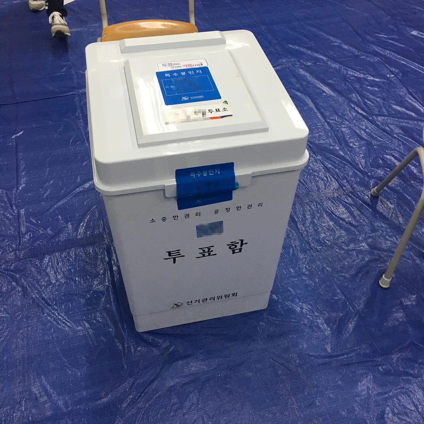 한국 선거에서 쓰는 흰 투표함. 앞면에 「투표함」과 선거관리위원회 표시가 있고 뚜껑에 봉인 스티커가 붙어 있다 (2016년 국회의원선거, 사진 revi, CC BY 2.0 KR, 위키미디어 공용)