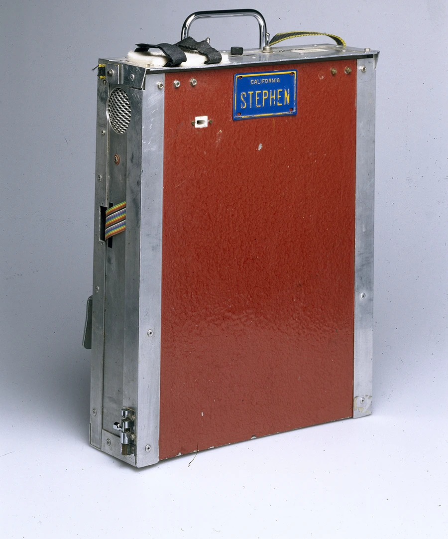 A metal housing containing the speech synthesizer and computer Hawking used. On a red plate is mounted a California license plate reading "STEPHEN." 1999, held by the Science Museum, London