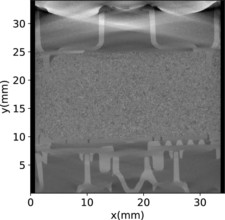 A vertical cross-section of an espresso capsule, imaged by X-ray micro-CT. The middle band, roughly 10–25 mm in height, is a layer of coffee grounds packed with fine particles, with the capsule's bright plastic and metal structures visible above and below it